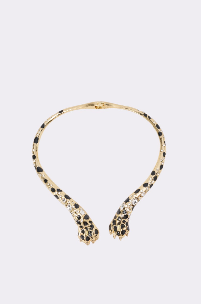 The I BITE NECKLACE is a gold-tone choker featuring black cheetah spots and paw-shaped ends, inspired by a leopard’s legs and paws, shown against a plain light background. 0