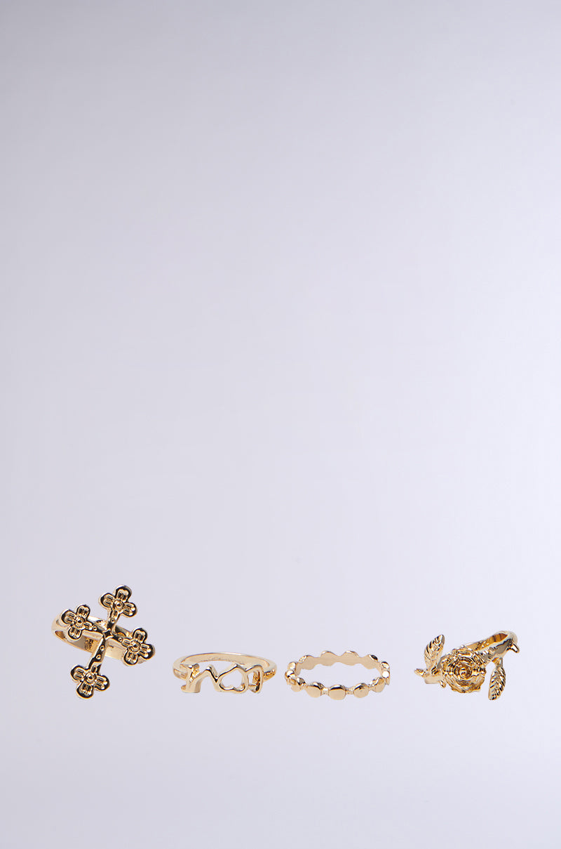 The CROSS YOUR HEART RING SET is elegantly displayed in a line against a light gray background, featuring faux gold rings with unique designs like floral patterns, interlocking loops, geometric shapes, and a bird motif. 1