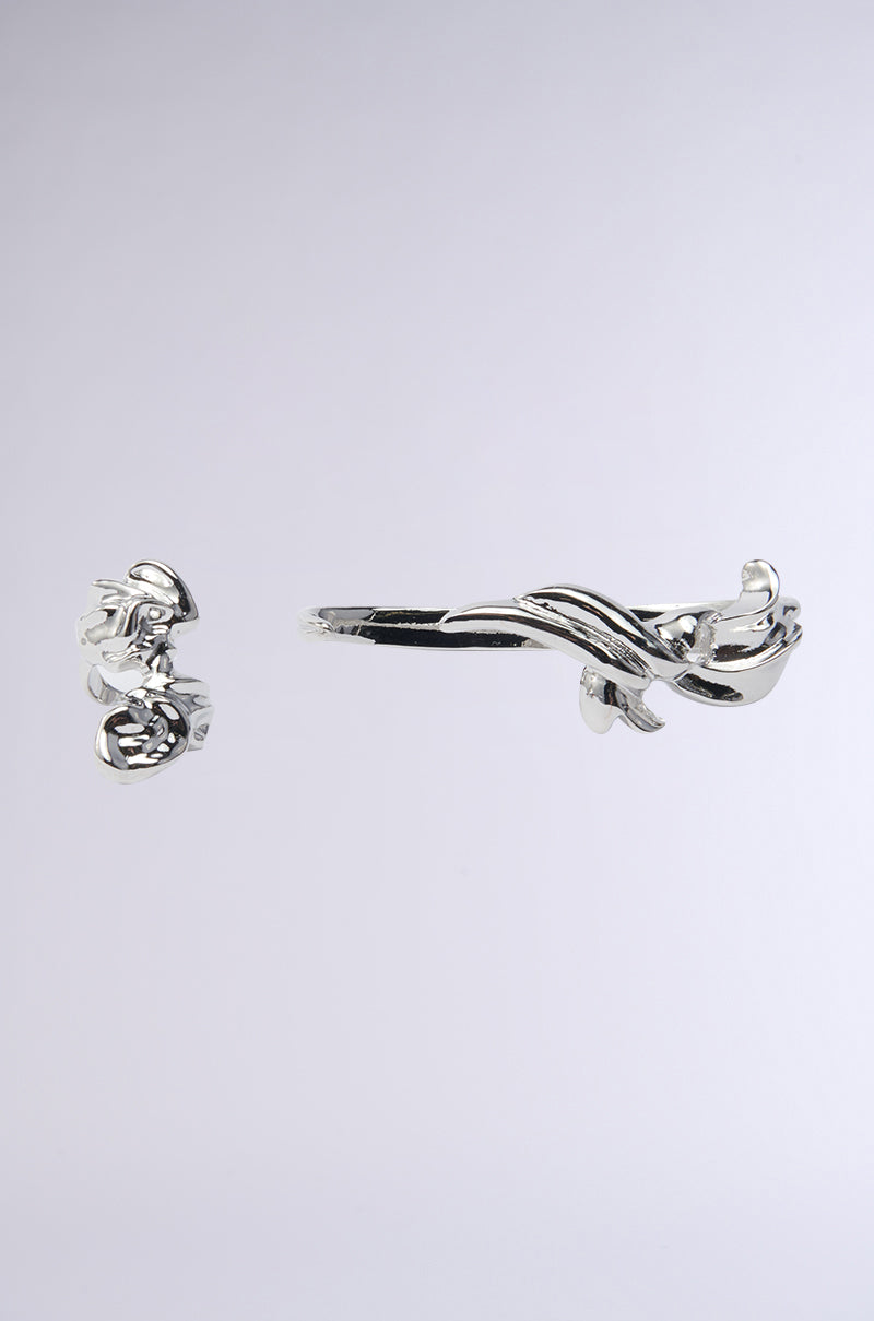 Silver ear cuffs are displayed on a plain backdrop, offering a futuristic vibe with sleek, flowing curves in an elegant pattern reminiscent of the ETHEREAL DREAMS HAND RING SET. The set includes both a cuff and matching ear piece. 0
