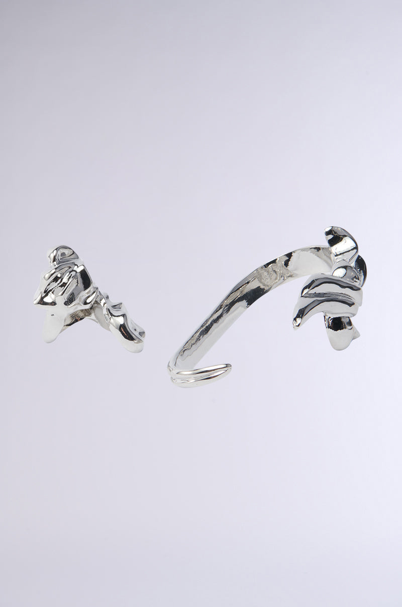 On a light gray background, abstract silver sculptures appear. The left object features a twisted, futuristic design with protruding elements. The right sculpture, resembling an Ethereal Dreams Hand Ring Set piece, is arch-shaped with curved extensions. Both have smooth and reflective surfaces. 2