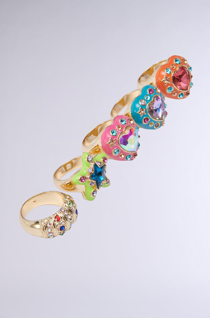 The FLOWER POWER RING SET includes five gold statement rings adorned with vibrant gems and fun shapes, arranged diagonally on a light gray background for a retro-inspired look.