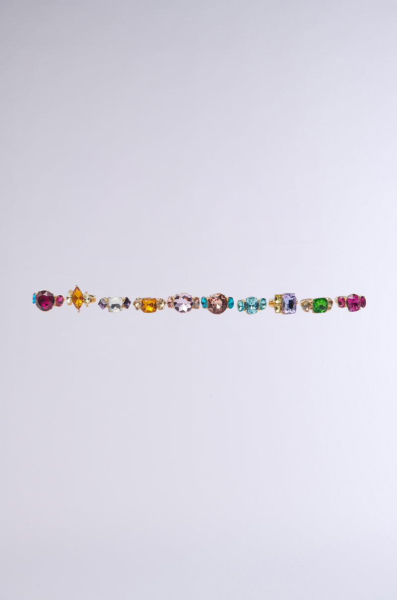 The SUMMER VIBES RING SET features a collection of rings adorned with vibrant, multi-shaped colorful gemstones, arranged in a single line against a plain light gray background.