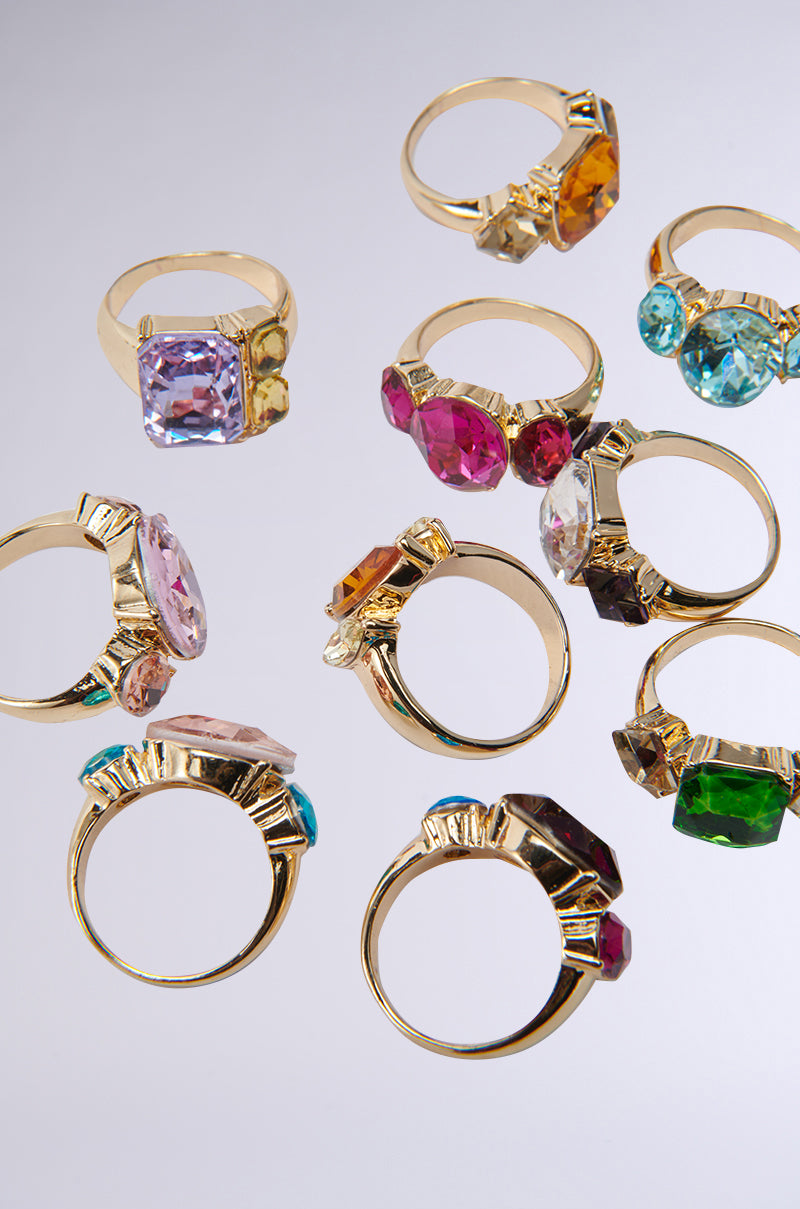 The SUMMER VIBES RING SET features gold-tone rings with oversized gemstones in pink, green, blue, amber, and purple hues, displayed on a light gray background—ideal for stacking or adding bold flair to your look.