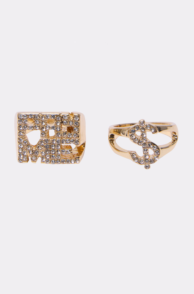 The PAY ME RING SET features two gold rhinestone rings: one spells "LOVE ME" in clear stones, and the other displays a rhinestone dollar sign ($), both sparkling brilliantly on a white background.