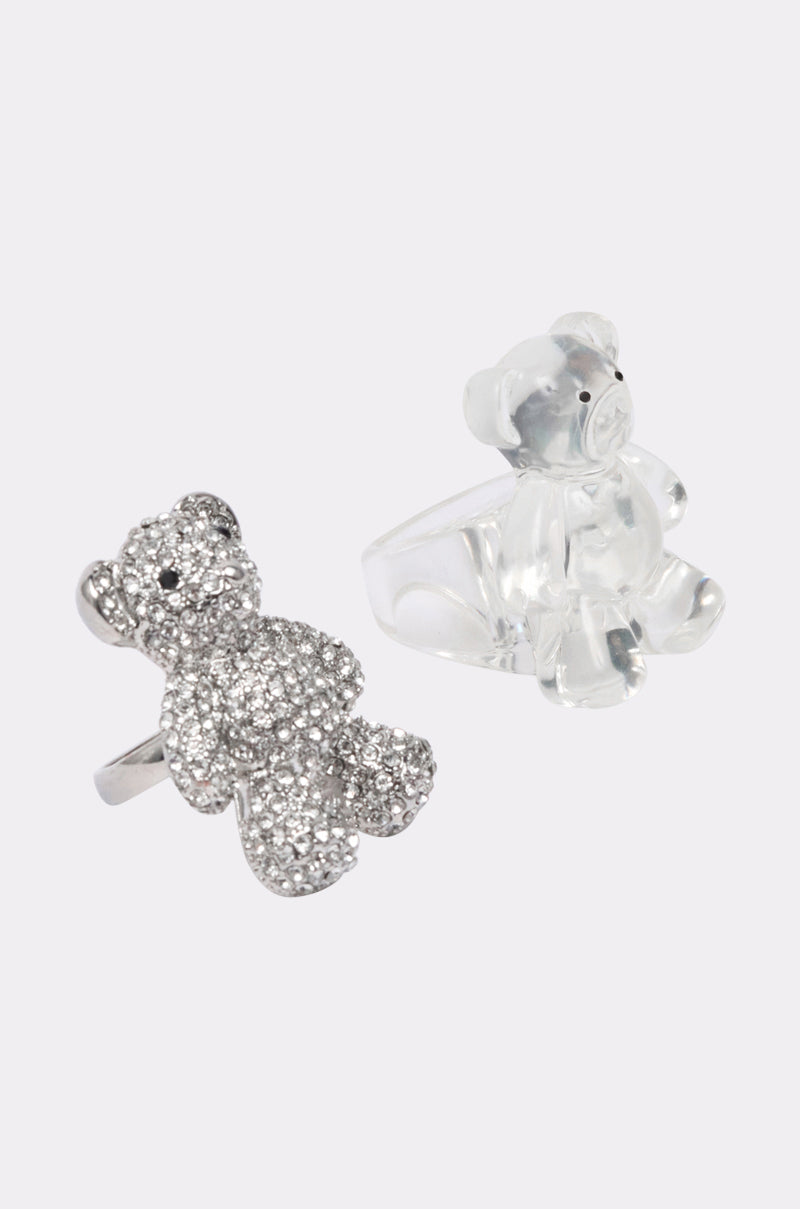 The SO CUDDLY RING SET features two teddy bear statement rings: one in sparkling silver rhinestones and the other crafted from clear material, both displayed on a plain, light background. 2