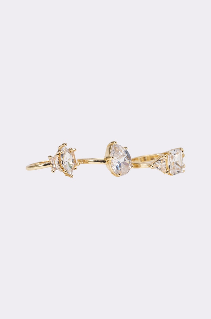 The TOP TIER RING SET features three uniquely shaped clear gemstones in pronged settings, arranged along a slim gold-tone band—a stylish choice for those who appreciate elegant jewelry. 2