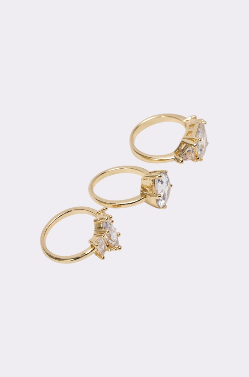 The TOP TIER RING SET features three gold-tone rings with large, clear rectangular gemstones set diagonally on a light background—an eye-catching choice for any formal jewelry collection. 3