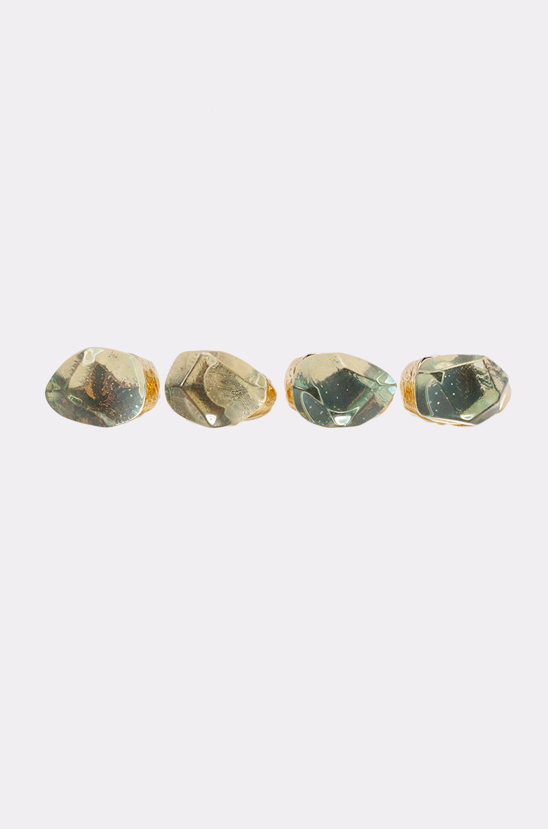 Four irregularly shaped, translucent green stones with gold-tone hammered bands are aligned in a row on a white background, showcasing the DONT BITE RING SET in a bold and eye-catching display. 1