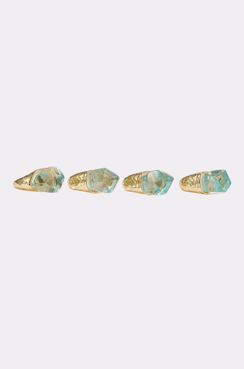 The DONT BITE RING SET features four gold-tone rings with large, light blue crystal-like stones displayed in a row on a clean white background, highlighting their bold and sparkling style. 2