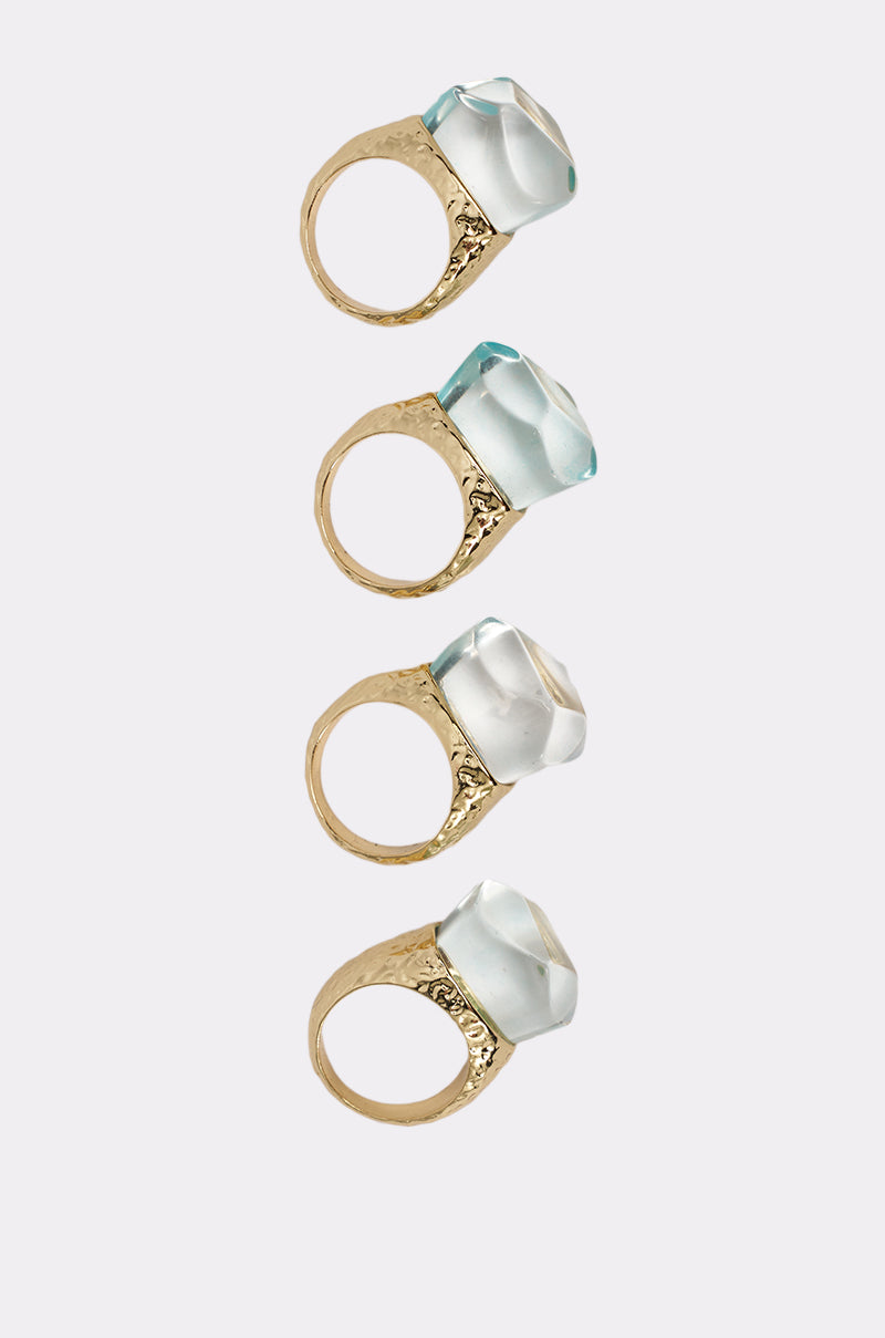 The DONT BITE RING SET features four gold-tone rings with large, faceted, translucent gemstones arranged vertically on a light gray background for an elegant look. 3