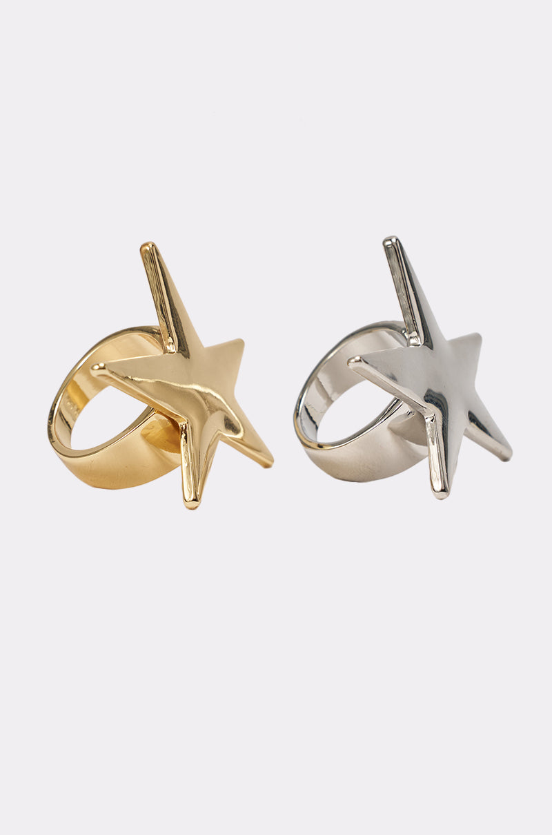 The IM THE STAR RING SET features two chunky mixed-metal rings with bold five-pointed star designs—one in shiny gold, the other in shiny silver—shown side by side on a plain white background. 3