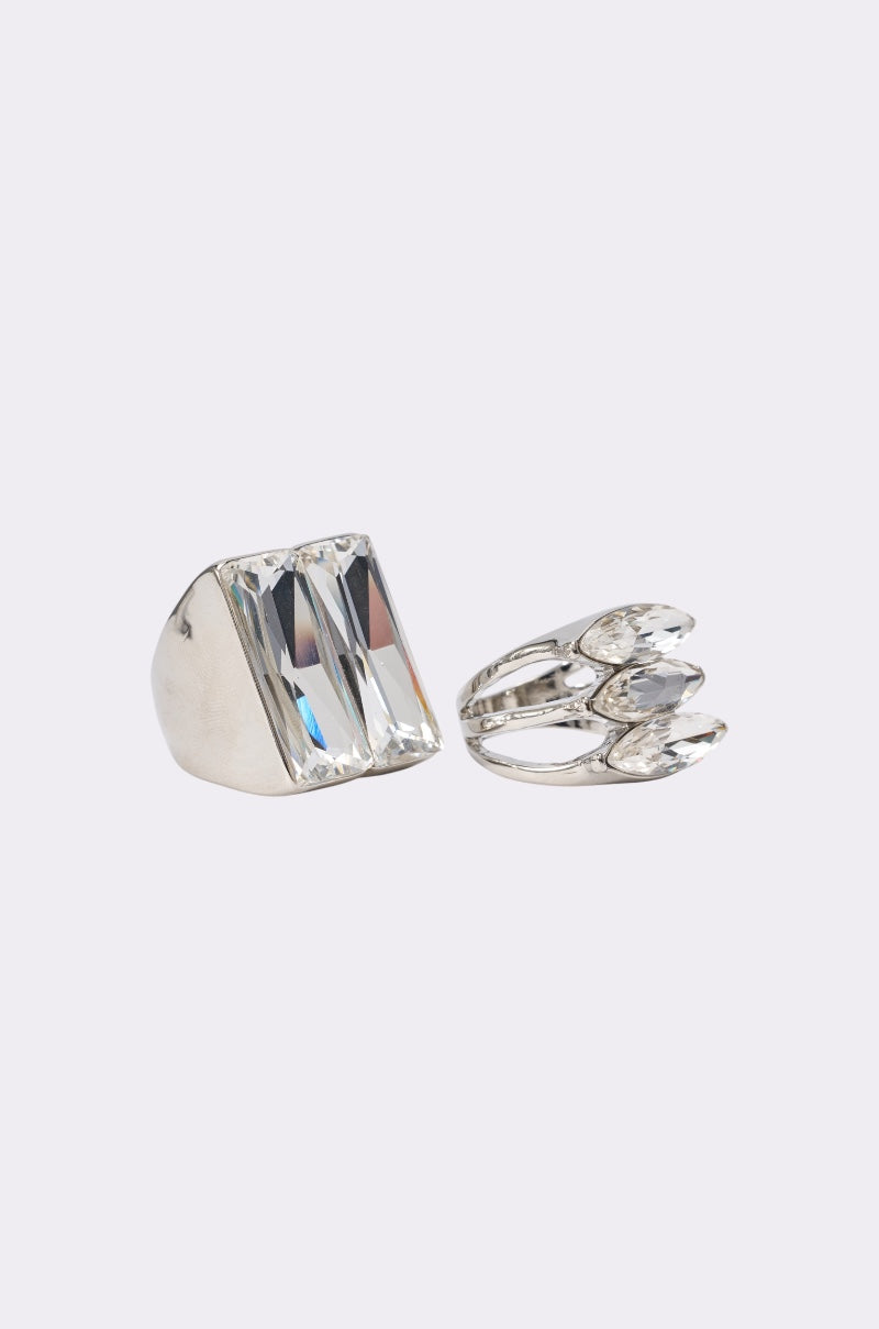 The RIRI RING SET features two silver statement rings: one with twin rectangular clear gemstones, the other with three overlapping oval-shaped stones—ideal for adding a glamorous, bold accent to any look. 2