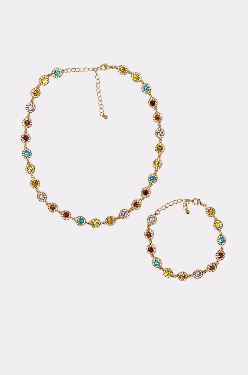 The COME CORRECT NECKLACE is a gold-tone necklace featuring round, multicolor faceted stones in yellow, turquoise, red, and white linked by small gold connectors, shown on a white background. 0