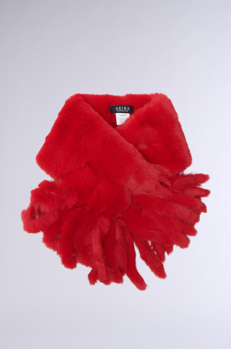 The IM EXTRA FAUX FUR SCARF, with its bright red hue and soft, fluffy texture, adds a vibrant pop to a plain background. It has fringed ends and includes a small "AKIRA" label in white text.