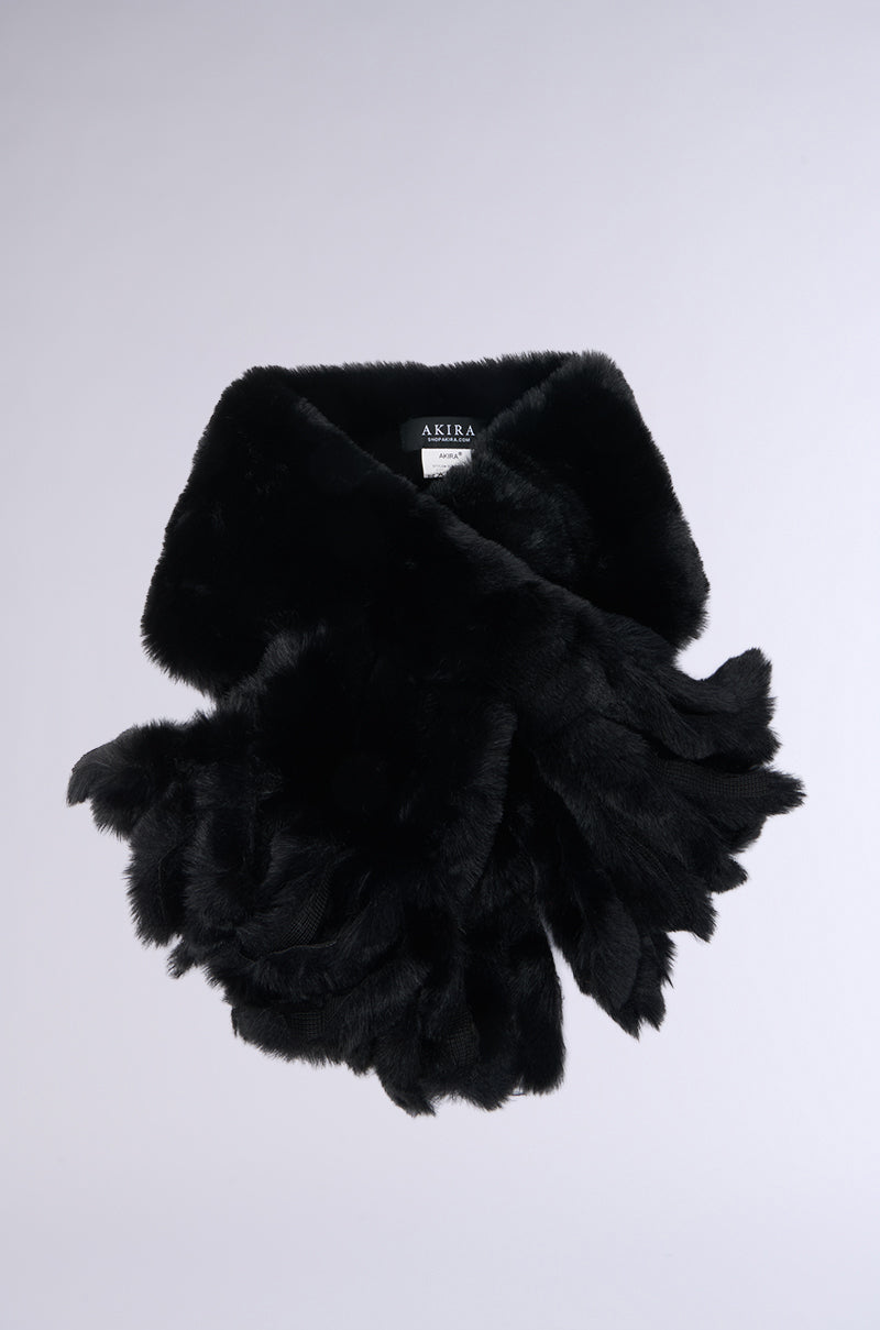 The EXTRA IS BETTER FAUX FUR SCARF, a luxurious black accessory with a soft and fluffy texture, is displayed on a light gray background. Ideal for monochromatic outfits, it features an overlapping design and a label sewn inside.
