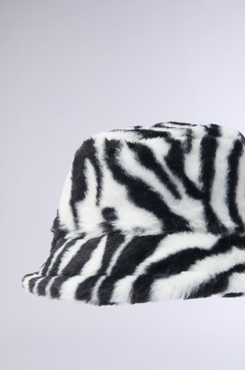 The WILD CHILD ZEBRA FAUX FUR HAT features a black and white zebra stripe pattern on a gray backdrop with adjustable drawstrings for the perfect fit. 4