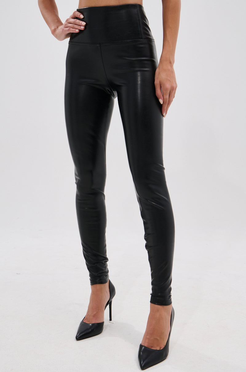 Wearing the SLIM THICC 4 WAY STRETCH LEGGING IN BLACK, styled with black pointed-toe heels, a person showcases the sleek bodycon fit against a plain white background.