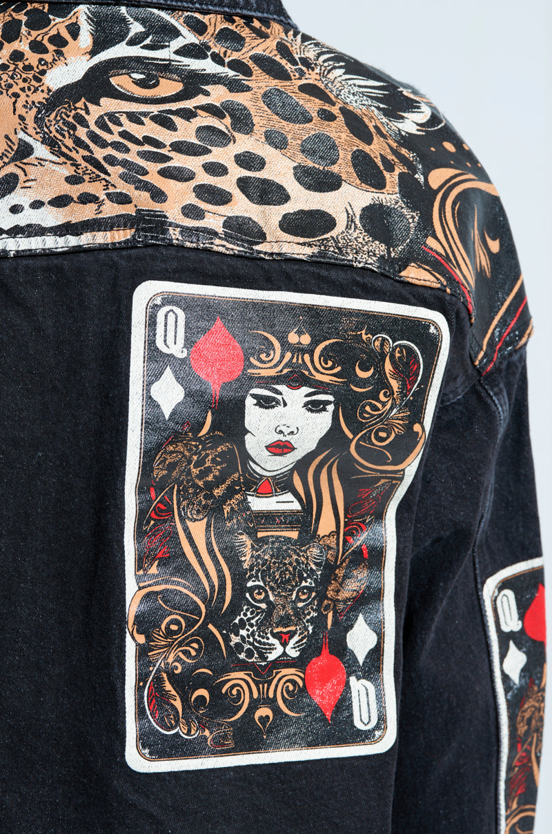 Close-up of the QUEEN OF HEARTS PRINTED AND EMBELLISHED DENIM JACKET in black, featuring vibrant playing card graphics on the back. It showcases a stylized Queen of Hearts with intricate patterns, a leopard head, red elements, and animal print accents on the shoulders.