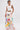 A woman with short slicked-back hair and arm tattoos stands against a white background wearing a 
