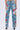 A rear view shows a person in INTO THE GARDEN FLORAL EMBROIDERED DENIM JEANS with colorful floral designs on the legs. The high-rise, light-wash denim is paired with white high-heeled shoes against a plain white backdrop.