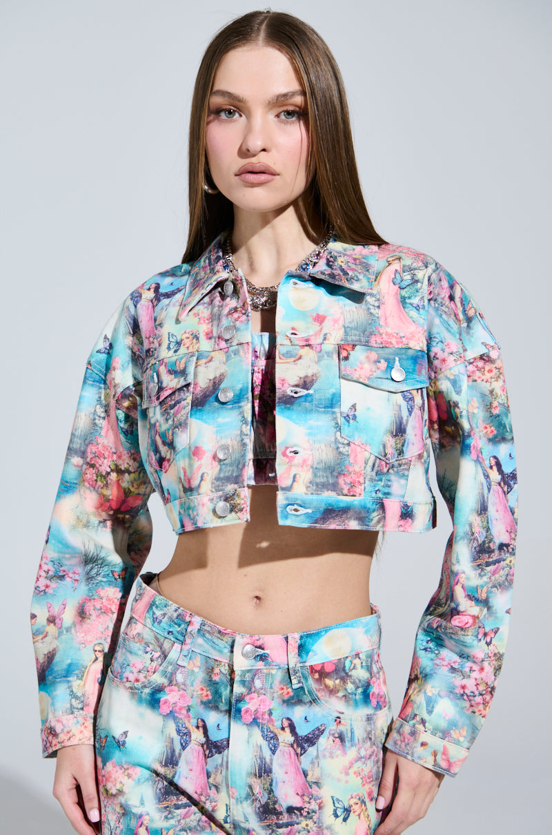 A person with long hair wears a FEMALE FANTASY PRINTED DENIM JACKET and matching pants, both featuring a vibrant, artistic pattern in candy colors. They stand against a plain background, their expression neutral yet intriguing.