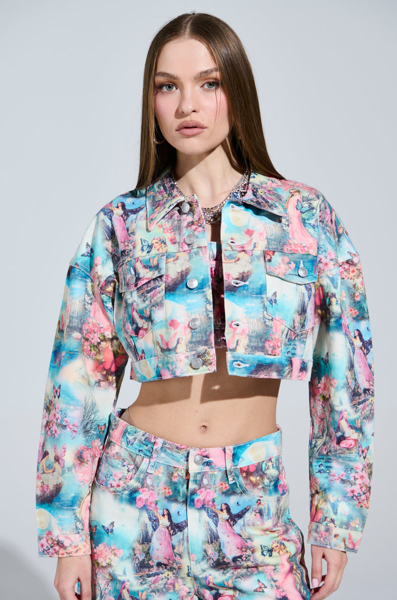 A person with long hair wears a cropped silhouette in candy-colored print. The jacket and matching high-waisted pants flaunt pastel illustrations, set against a softly lit background, creating a dreamy vibe like a FEMALE FANTASY PRINTED DENIM JACKET ad.