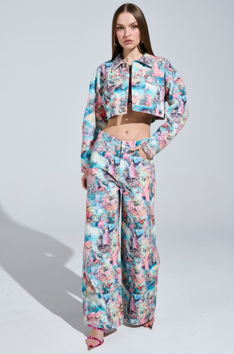 A woman poses against a plain background in a whimsical fairy-like ensemble, wearing the long-sleeved, cropped Female Fantasy Printed Denim Jacket with wide-leg pants. Her flowing hair complements the candy-colored outfit as she poses with one hand on her hip.