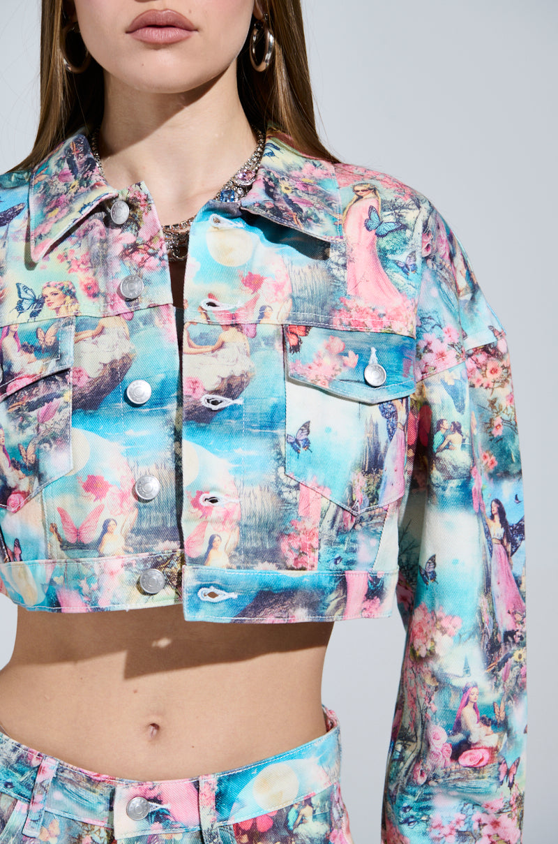 A person wearing a candy-colored FEMALE FANTASY PRINTED DENIM JACKET with whimsical fairy vibes shows fairytale scenes of castles, princesses, and butterflies. This vibrant cropped jacket with silver buttons is paired with matching bottoms on a plain gray background.