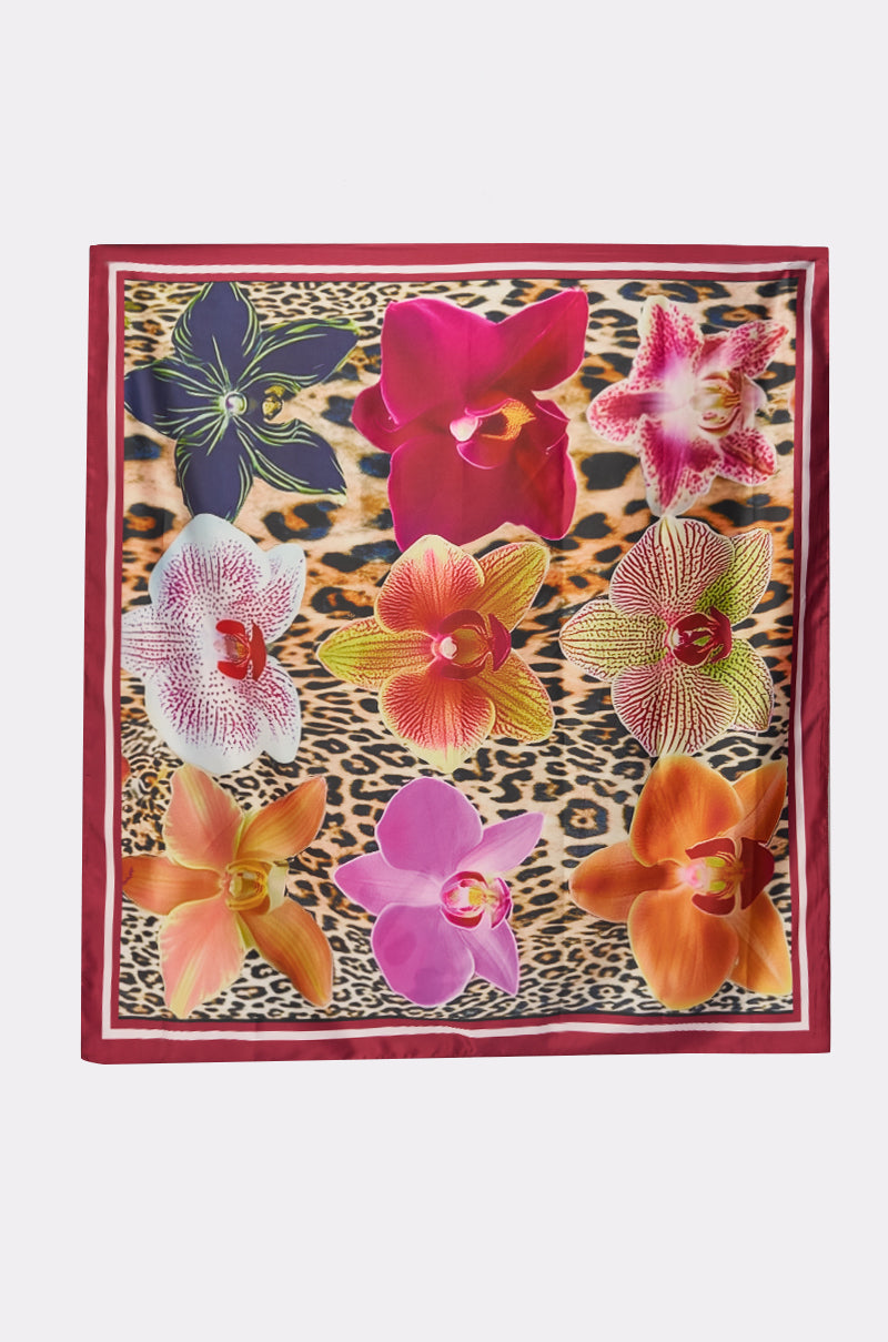 The WILDLY FEMME SATIN SCARF features a leopard-print background, red border, and nine vibrant orchid flowers arranged in a striking grid pattern. 3