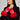 A person wearing a black coat with large red faux fur cuffs and the ALL I WANT IS MONEY FUR GLOVES stands against a plain background. They have long dark hair, are looking to the side, and don stylish large hoop earrings.