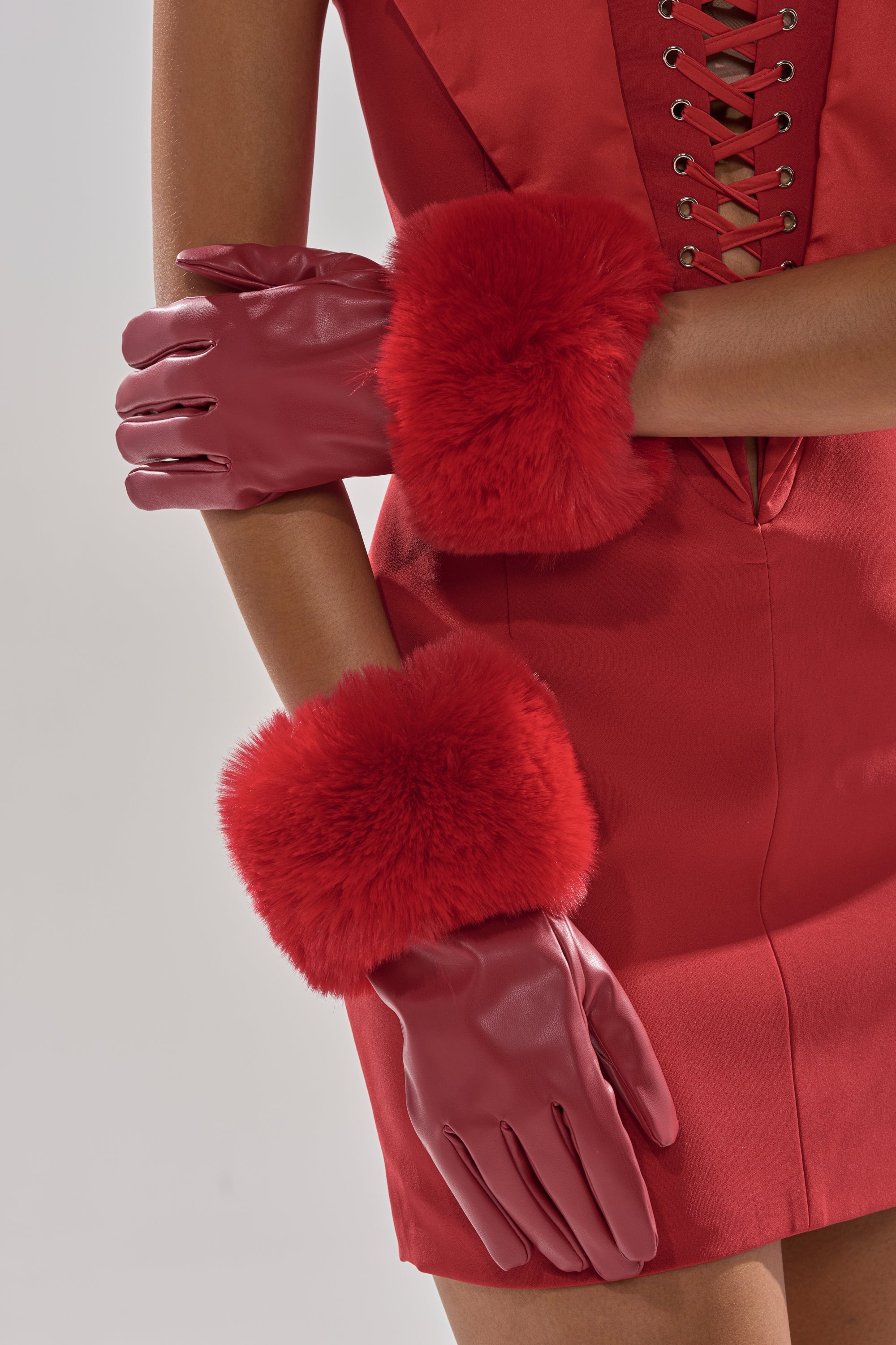 A person with arms crossed wears the ALL I WANT IS MONEY RED FUR GLOVES—red gloves with fluffy fur cuffs—paired with a red lace-up dress, shown from shoulders to mid-thigh against a light background. 1