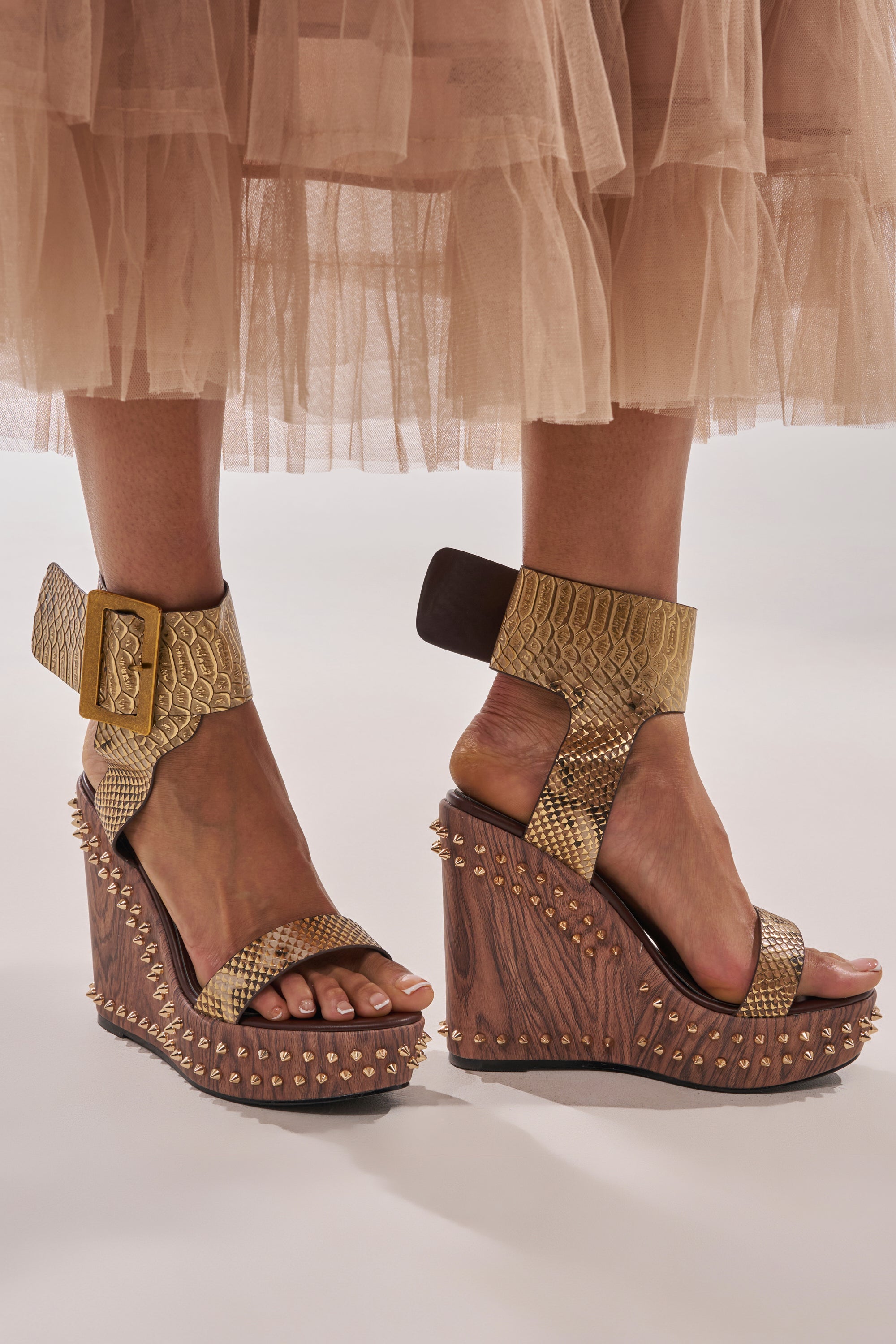 Someone wearing the AKIRA GOLD SLOANE BROWN STUD AND SNAKE WEDGE SANDAL with a layered beige tulle skirt. 0