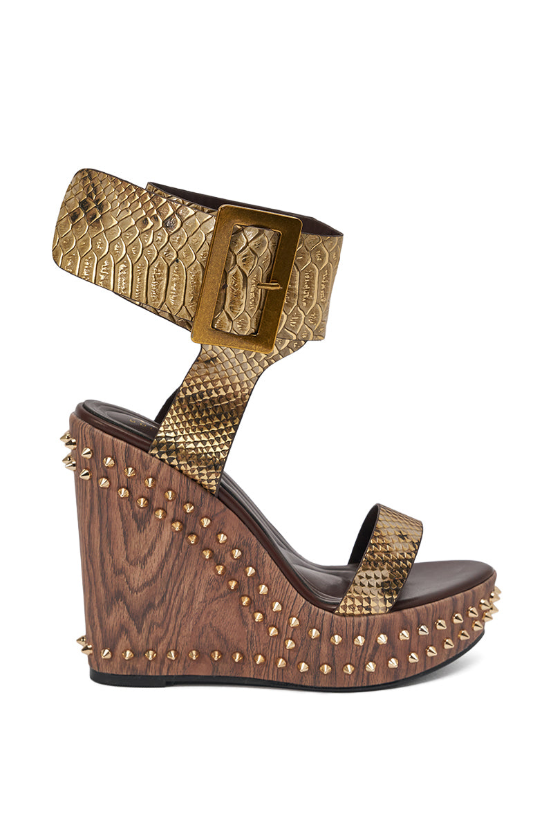 The AKIRA GOLD SLOANE BROWN STUD AND SNAKE WEDGE SANDAL features gold metallic snakeskin, a platform sole, a large matching buckle, and gold spike studs accenting the base and wedge. 3