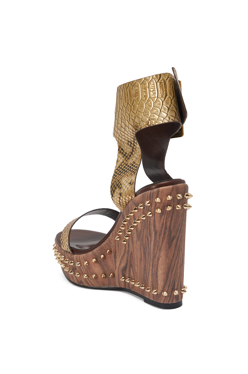 The AKIRA GOLD SLOANE BROWN STUD AND SNAKE WEDGE SANDAL features a high platform sole, metallic snakeskin-textured gold ankle strap, and decorative gold studs on a faux wood heel. 5