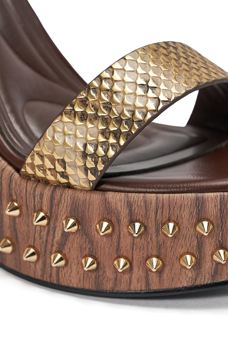 Close-up of the AKIRA GOLD SLOANE BROWN STUD AND SNAKE WEDGE SANDAL, showcasing a textured metallic snakeskin gold strap, wooden platform sole, and gold studs for a modern, edgy look. 6