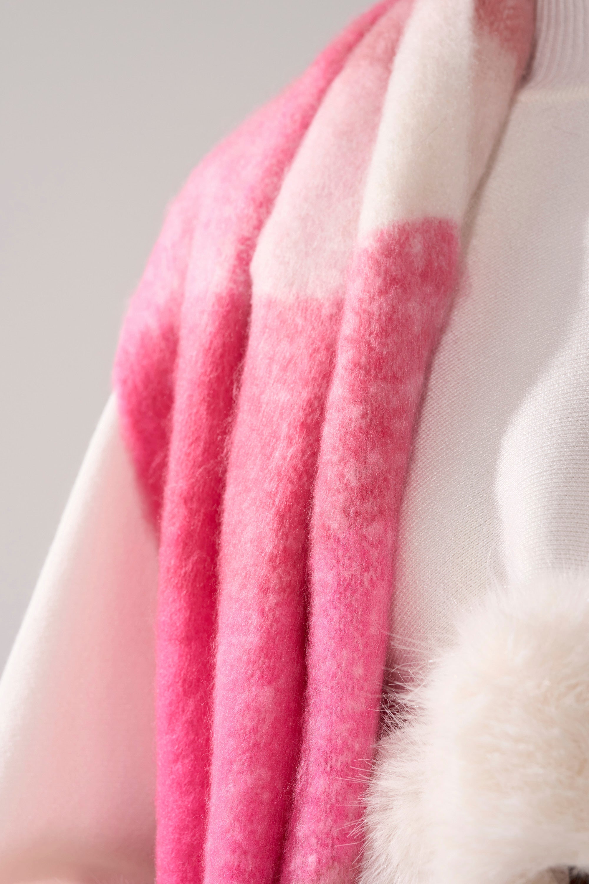 A close-up of a person wearing the IN MILAN BLANKET SCARF in soft pink and white over a white top, with a fluffy white accessory visible at the bottom right. 3