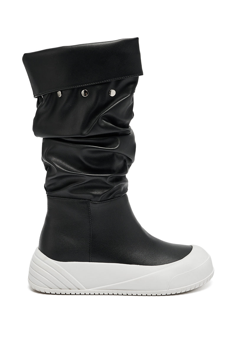 The AZALEA WANG SMARTER BLACK RUCHED PU FLAT BOOT features a black ruched design, slouchy folded shaft with silver studs, and a thick white textured flat sole.
