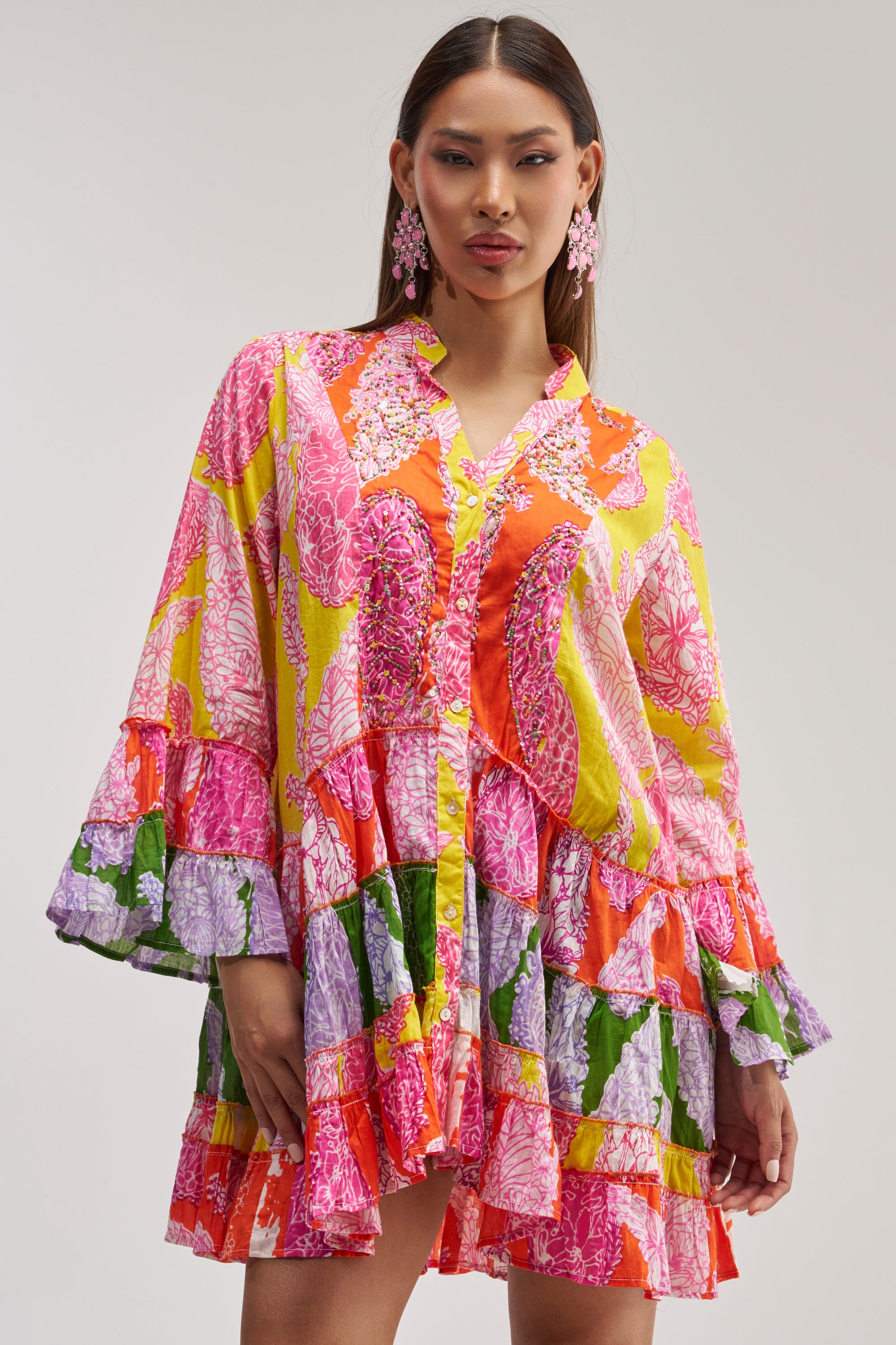 A woman poses confidently against a plain background wearing the DANCING TILL SUNRISE FLORAL LONG SLEEVE DRESS, a colorful mini dress featuring vibrant pink, orange, yellow, green, and purple patterns.