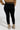 A person wearing a brown sweater, SNUGGLE FLEX FLEECE LEGGING EXTENDED SIZE IN BLACK, and beige boots is standing with their back facing the camera against a plain background.