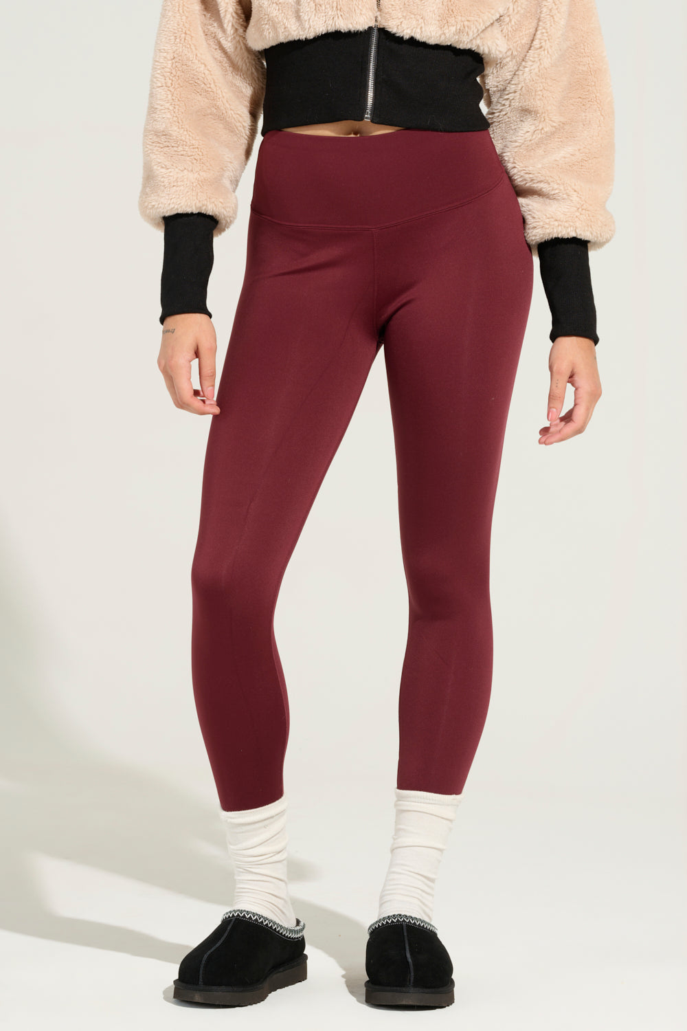 A person wearing Snuggle Flex Fleece Leggings in Red, a cropped beige sweater, white socks, and black slip-on shoes. The image highlights their lower body against a plain background. 0