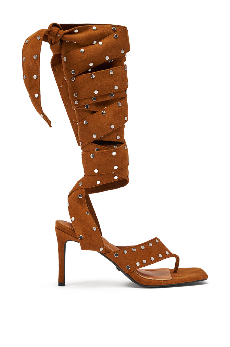 The AZALEA WANG SODALITE COGNAC STRAPPY FAUX SUEDE SANDAL is a brown faux suede, open-toe sandal with long wraparound straps and studded heels, designed to lace up the leg. 2