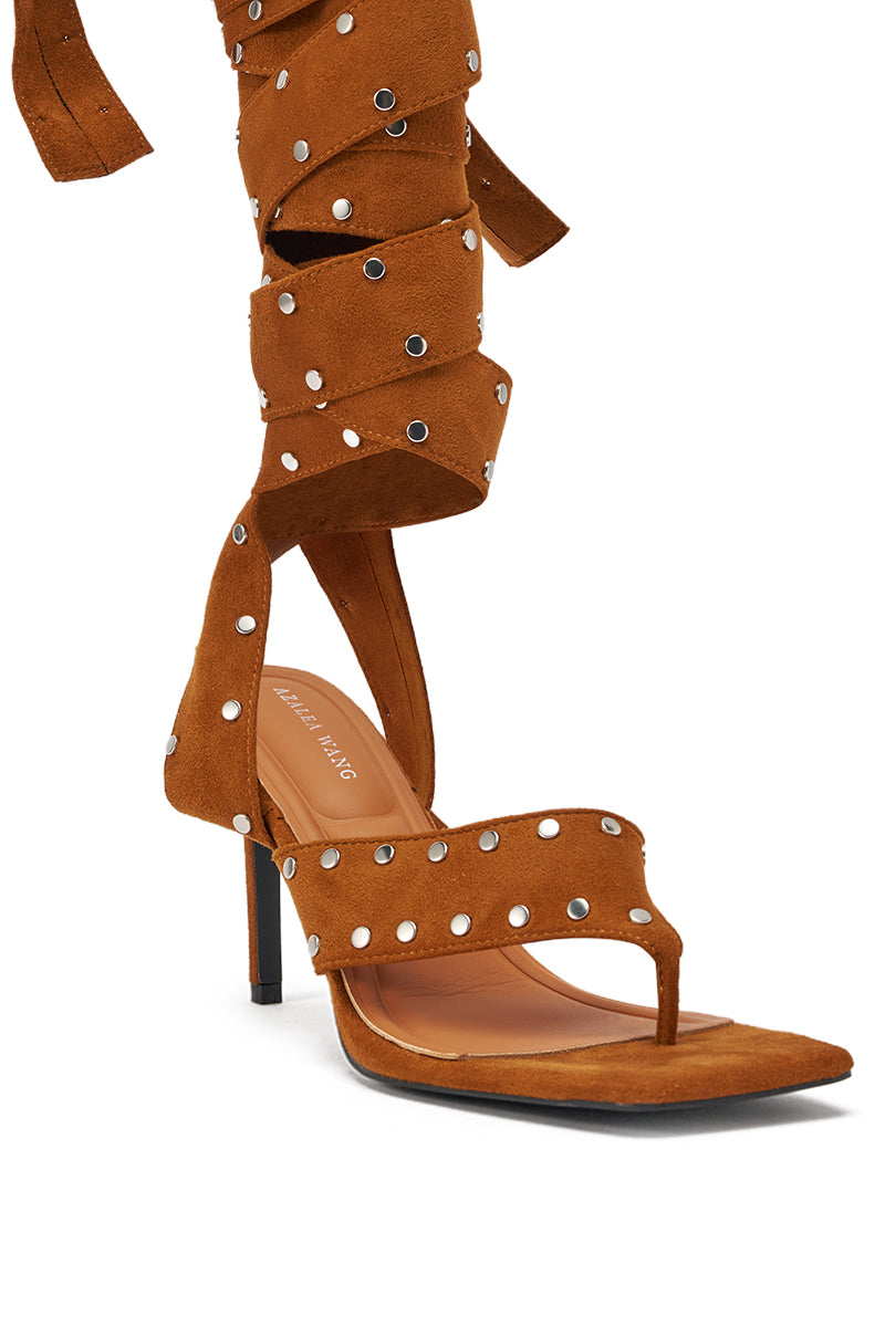 The AZALEA WANG SODALITE COGNAC STRAPPY FAUX SUEDE SANDAL features brown faux suede, a thong toe, ankle strap, long studded wraparound laces, an open design, and a slender heel for a chic look. 5