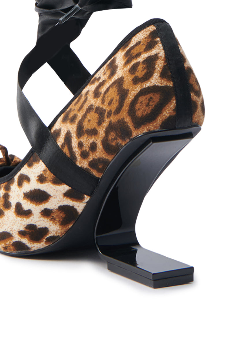 The AZALEA WANG SOLANA LEOPARD WEDGE PUMP features an eye-catching design with a glossy black inverted wedge heel and angular form. A suede textile upper with sleek black straps across the foot complements the bold leopard print.
