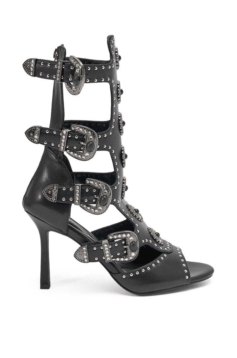 The AKIRA GOLD SOLVEIG BLACK EMBELLISHED WESTERN STILETTO SANDAL features black gladiator styling with multiple straps, silver studs, and bold western buckles at the front and ankle. 2