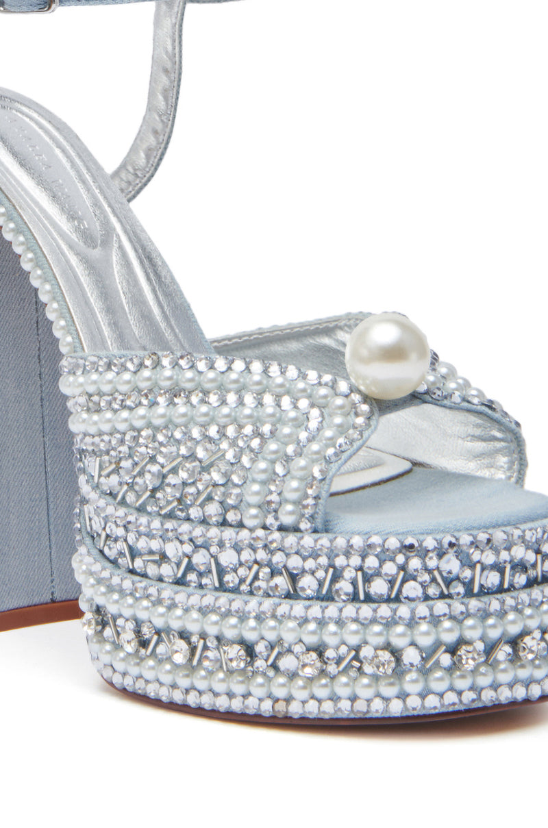 A close-up of the AZALEA WANG SOMETHING BLUE CHUNKY SANDAL, a light blue denim high-heeled sandal adorned with pearl and rhinestone embellishments, a large pearl-accented strap, and finished with a metallic silver insole.