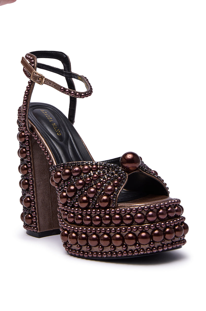 The AZALEA WANG SOMETHING BRONZE EMBELLISHED PLATFORM SANDAL features a brown velvet finish, faux leather details, rows of shiny brown beads and pearls, an embellished heel, ankle strap, and open toe design.