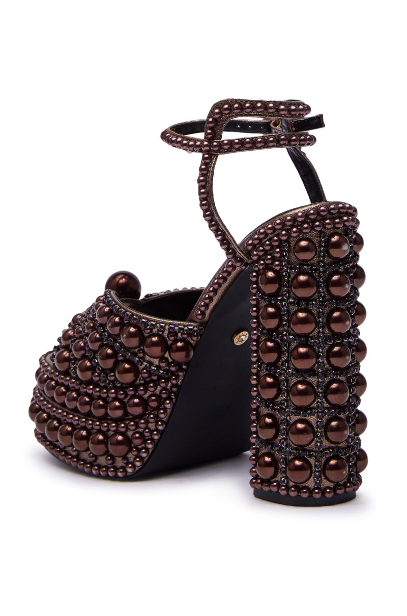 The AZALEA WANG SOMETHING BRONZE EMBELLISHED PLATFORM SANDAL features a high heel, chunky platform, ankle strap, and is adorned with shiny dark brown beads and bronze pearls for a bold, ornate look.