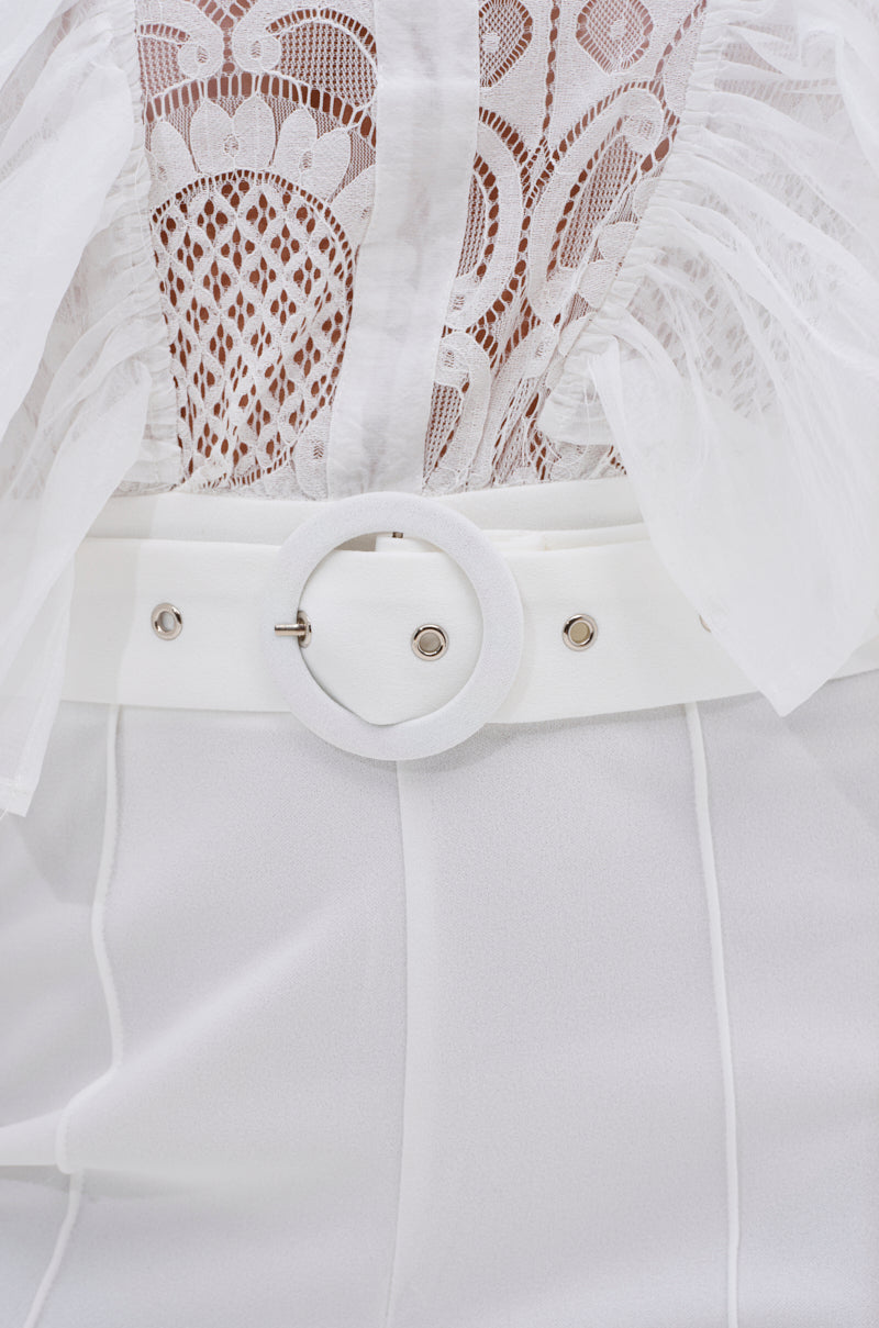 Close-up of the WALK THAT WALK RUFFLE JUMPSUIT IN WHITE, showcasing a sheer lace top with intricate patterns and feather details, high-waisted wide-leg pants, and a wide white belt with a large round buckle.