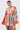 A woman wears the CRAZY IN LOVE SATIN ROMPER, featuring a baroque print, long flowy sleeves, and a deep V-neckline. She holds a woven handbag while standing against a plain white background.