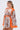 Woman in the CRAZY IN LOVE SATIN ROMPER, a vibrant baroque scarf-print piece with wide orange sleeves, styled with hoop earrings and a low ponytail, posing at an angle against a plain white background.